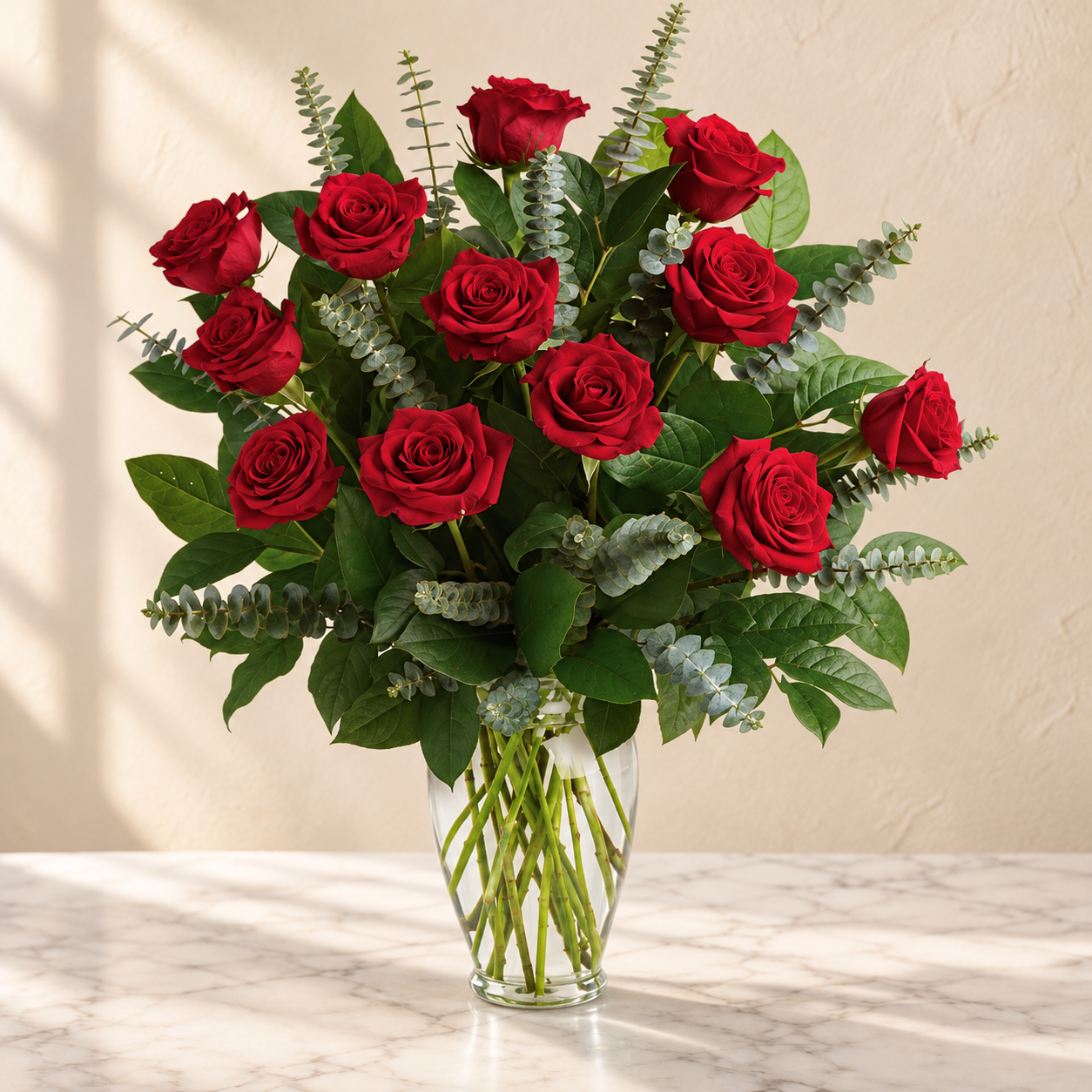 A dozen red roses with eucalyptus and lemon leaf in a tall clear glass vase