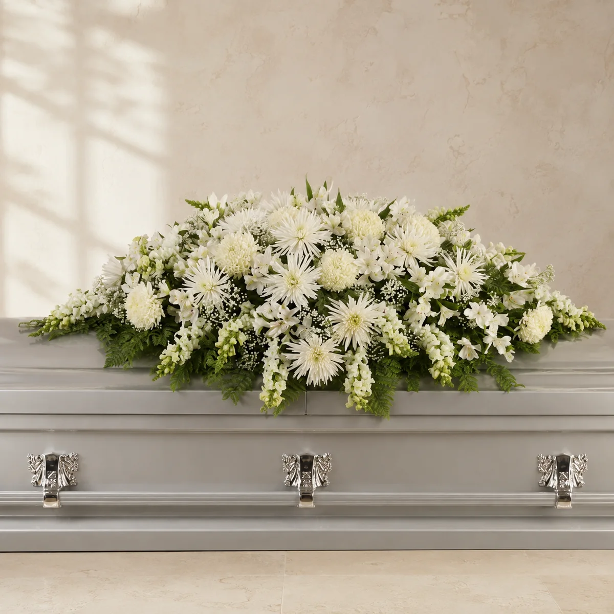 Cream white and ivory casket spray arranged across a closed silver casket