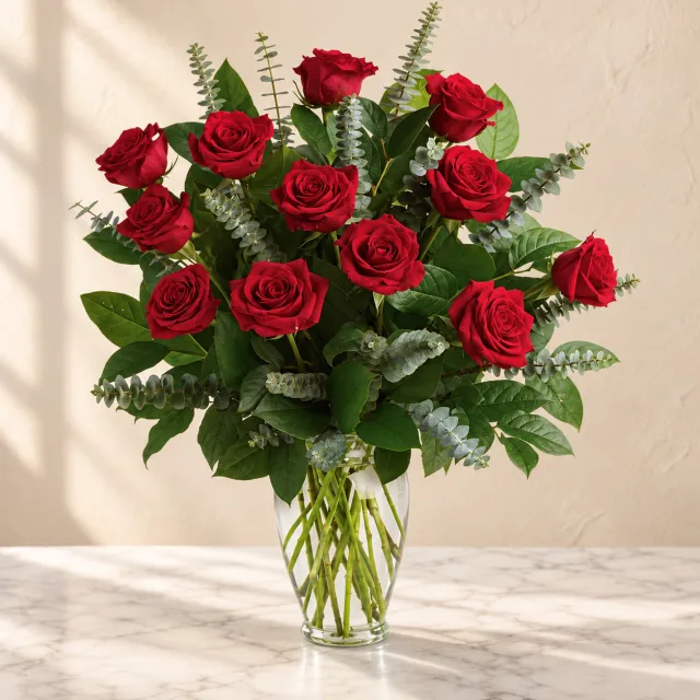 Red roses with eucalyptus and lemon leaf in a tall clear glass vase