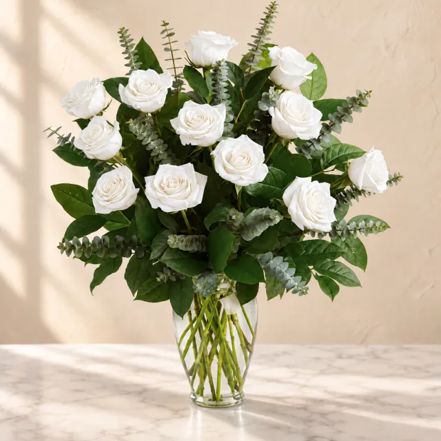 White roses with eucalyptus and lemon leaf in a tall clear glass vase