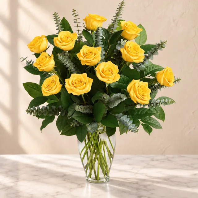 Yellow roses with eucalyptus and lemon leaf in a tall clear glass vase
