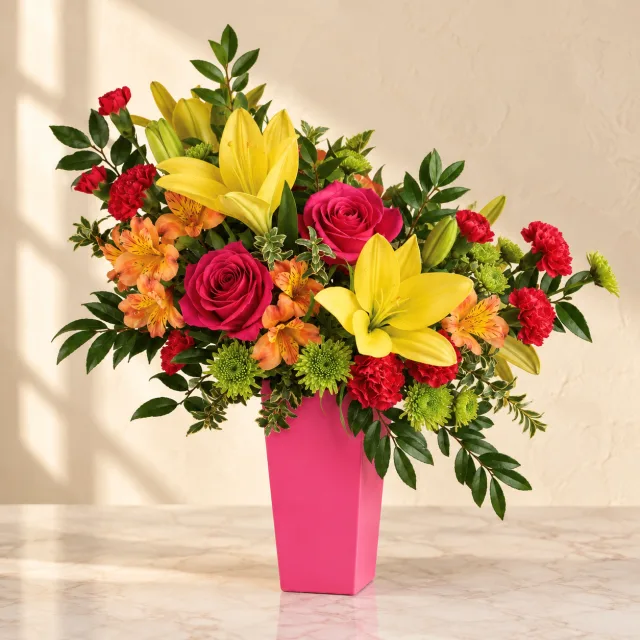Hot pink roses, yellow lilies, orange alstroemeria and red carnations in a tapered hot-pink vase