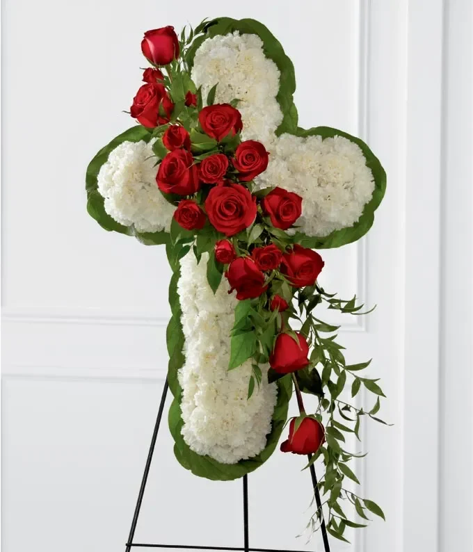 Red carnation and rose floral cross with a cream-white border on a standing easel