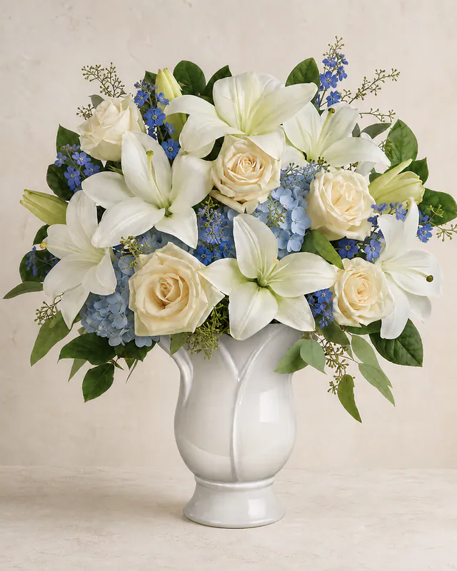 Natural powder-blue flowers with cream-white lilies and ivory roses in a ceramic vase